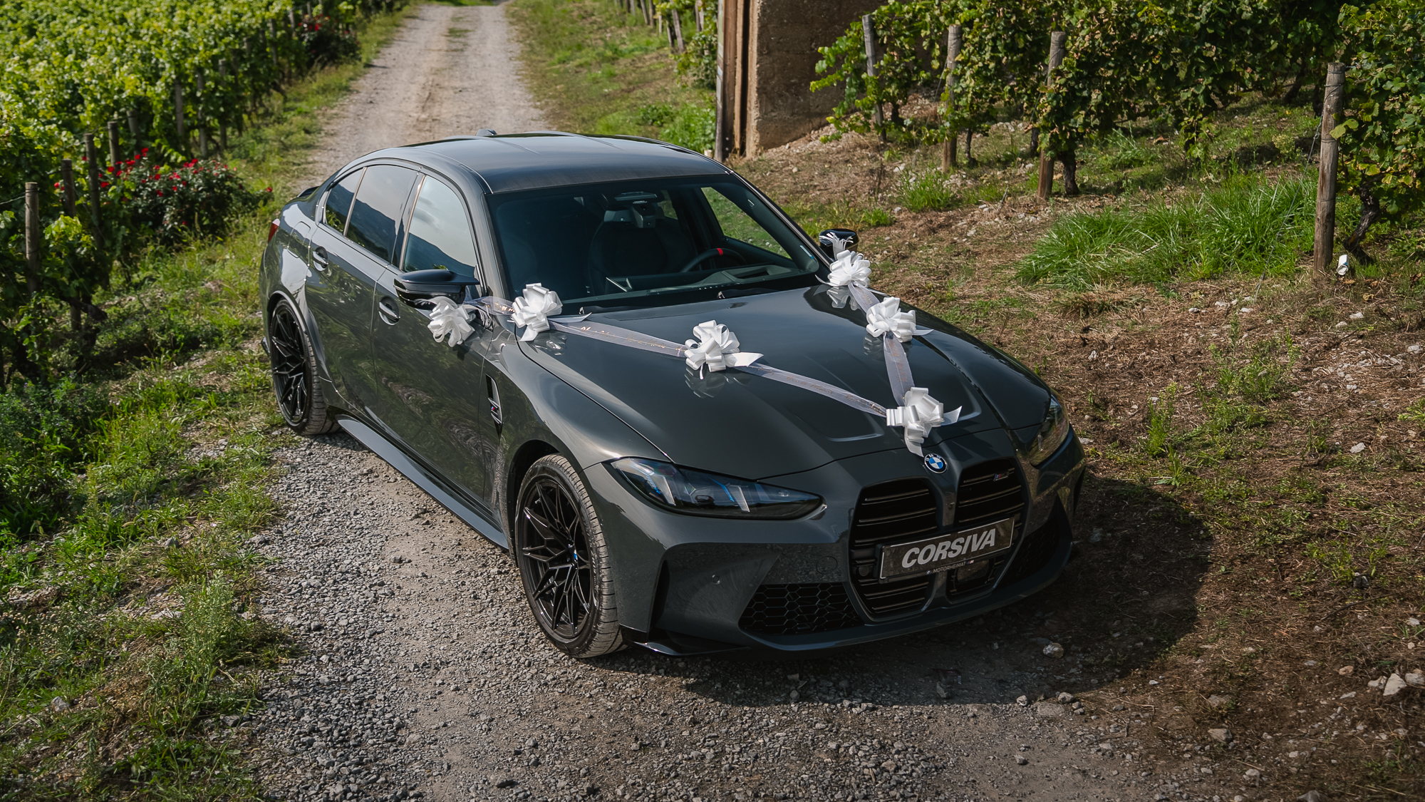 BMW M3 Competition décorée de rubans blancs pour un mariage, vue de trois quarts avant