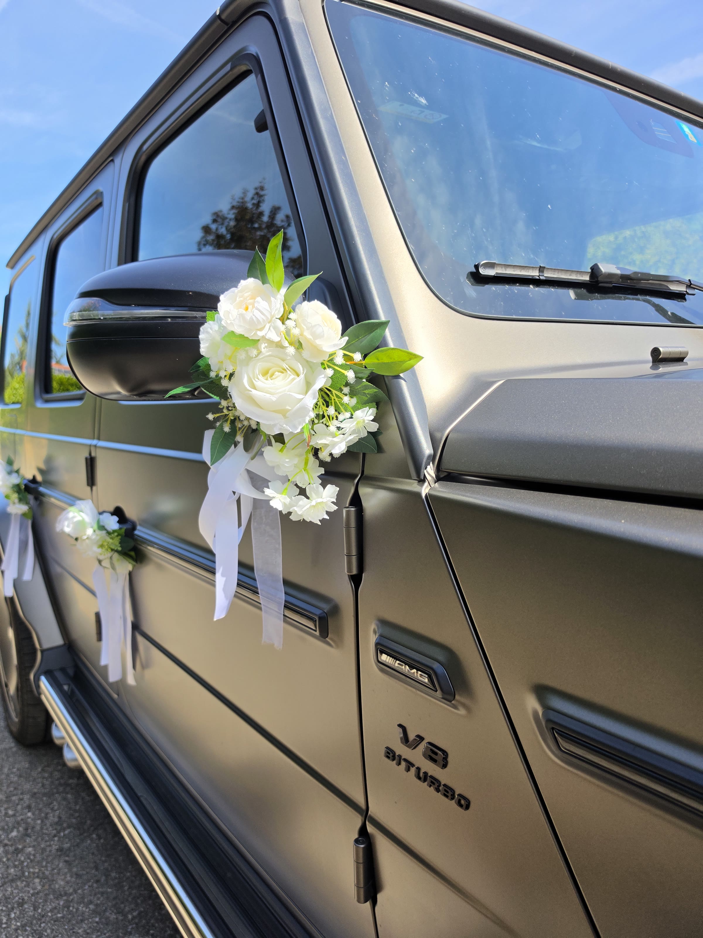 Bouquet de fleurs blanches et rubans noués sur le rétroviseur du Mercedes Classe G 63 AMG 2025, badge V8 biturbo
