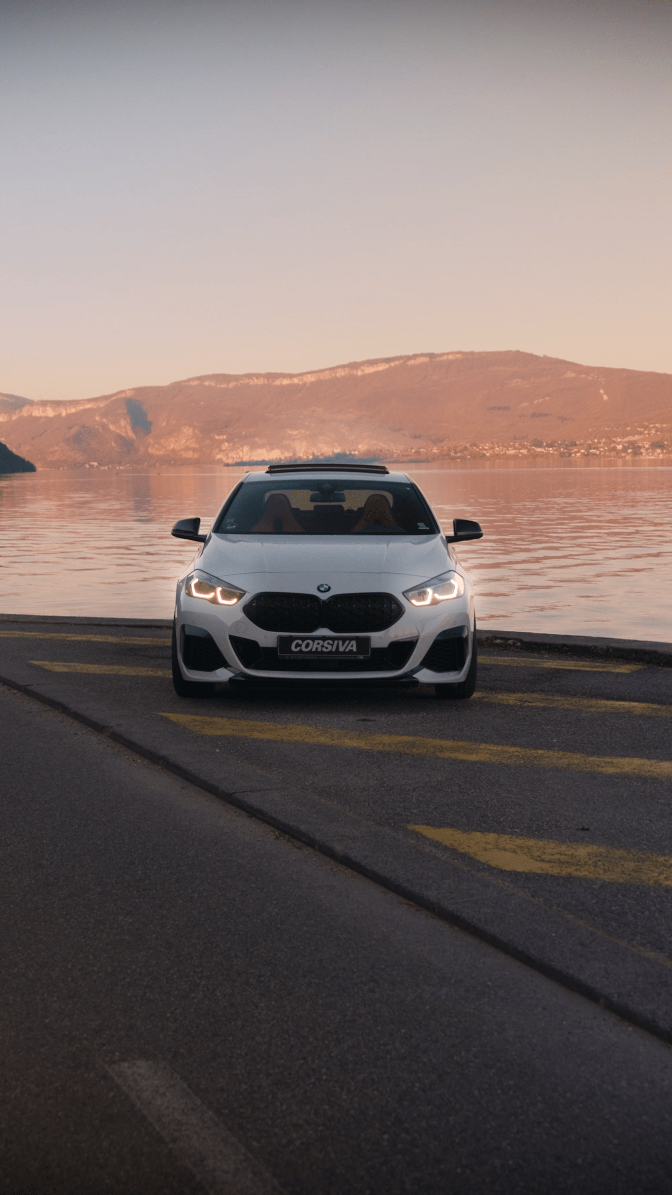 BMW M235i blanche de face, lac au coucher du soleil