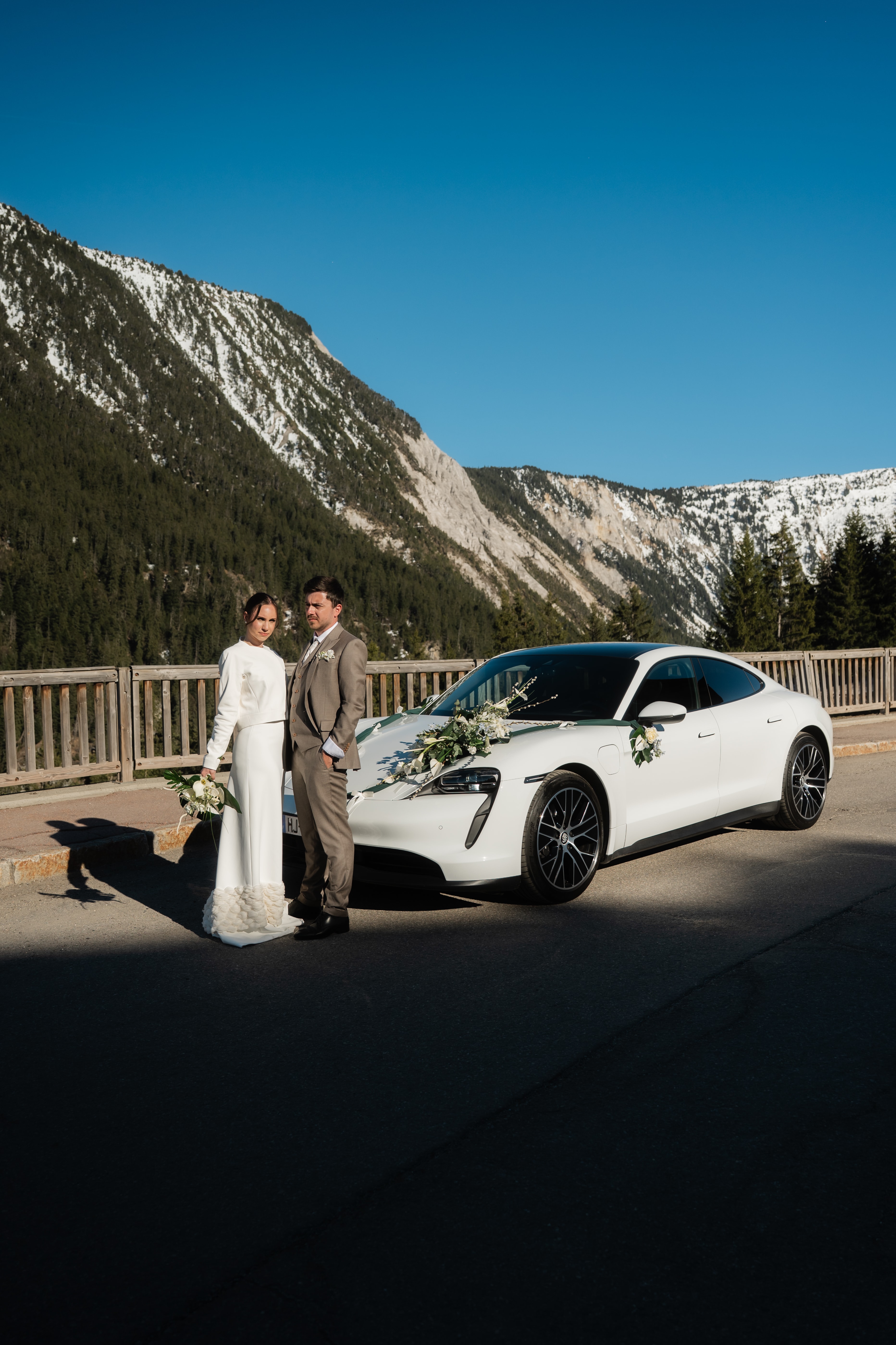 Les mariés main dans la main devant la Porsche Taycan blanche fleurie